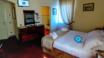 A hotel room with a bed, a desk with a computer, a TV, and a bathroom visible through an open door.