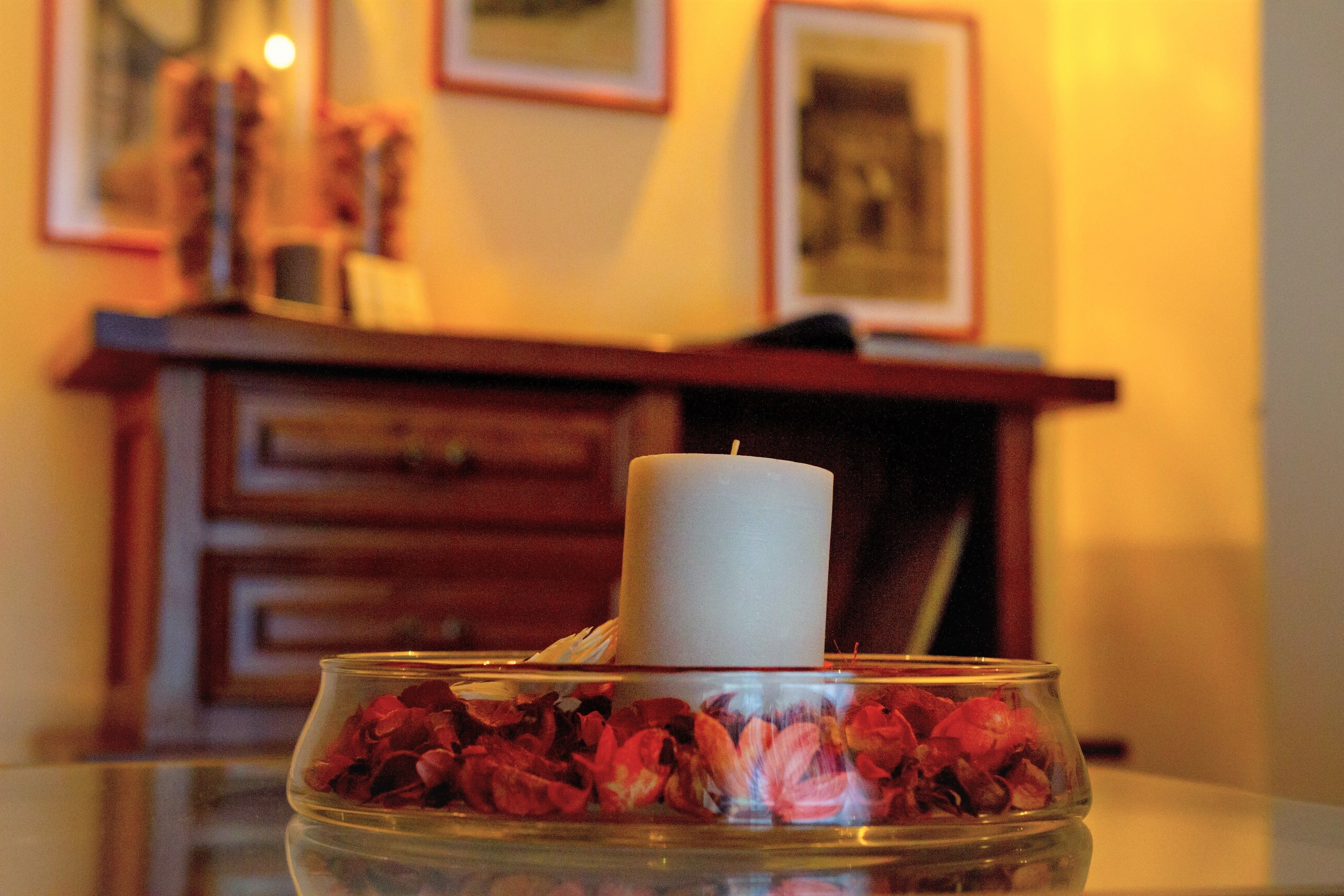 Ein Teelicht in einem Glasgefäß mit Rosenblättern auf einer spiegelnden Oberfläche.