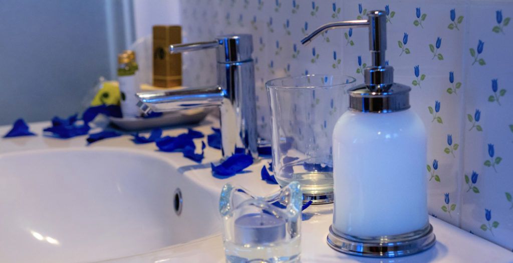 Un lavabo de salle de bain avec un robinet moderne, un pichet en verre et un distributeur de savon.