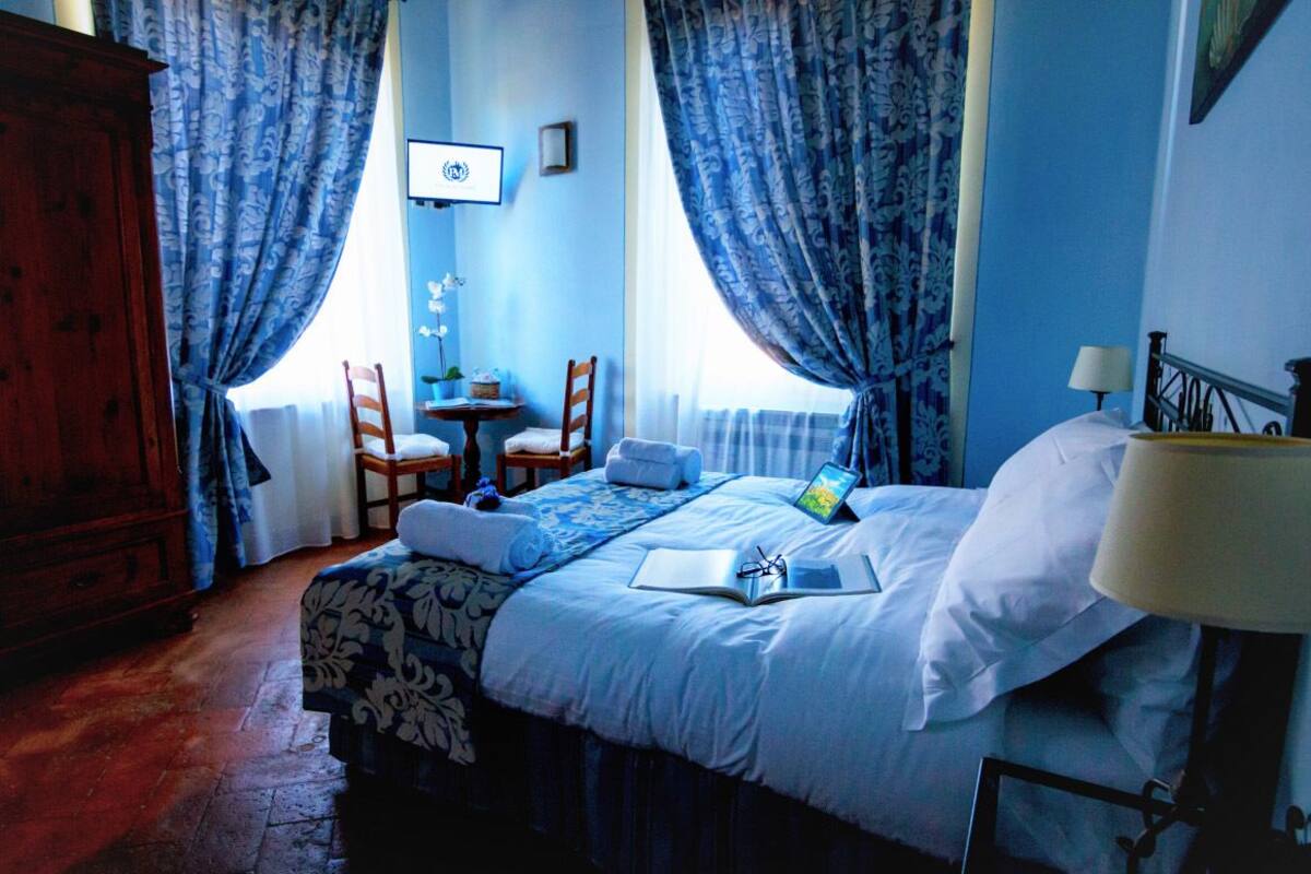 Quarto com uma cama, uma escrivaninha, duas cadeiras, uma televisão e uma janela com cortinas.