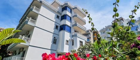 Een hotel met meerdere verdiepingen en balkons, omringd door weelderig groen en kleurrijke bloemen.