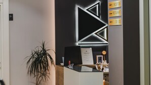 A reception desk with a modern design, a security camera above it, and directional signs for the reception and restaurant. - Hotel Alpha (Sarandë)