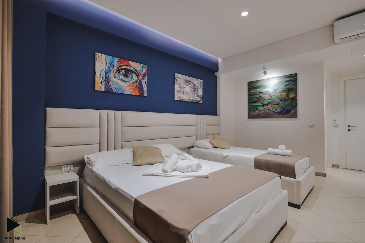 A hotel room with two beds, a headboard, artwork on the walls, and a door.