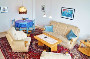 Un salon comprenant un canapé, des fauteuils, une table basse, une table à manger avec des chaises et un tapis à motifs.