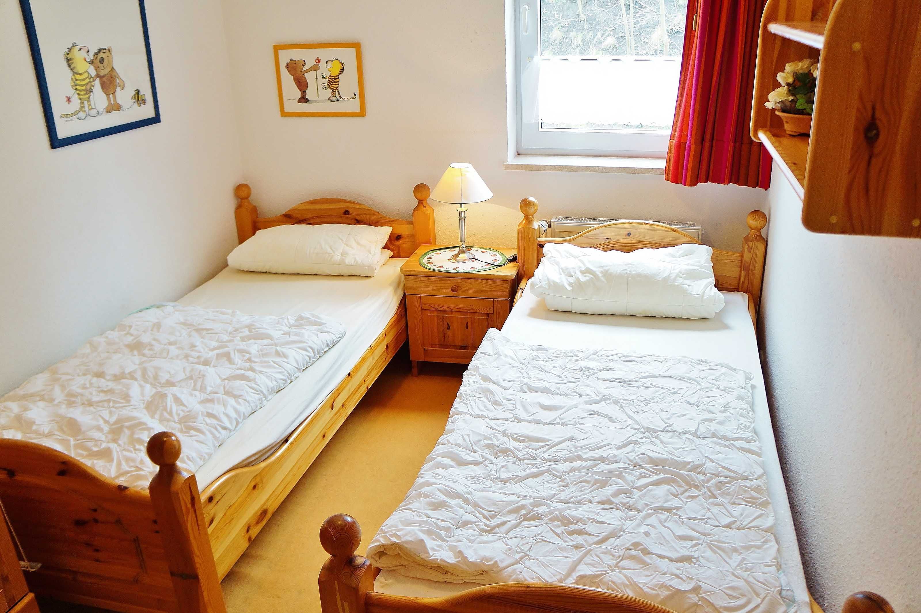 A room with two wooden beds, a nightstand with a lamp, and a window with curtains.