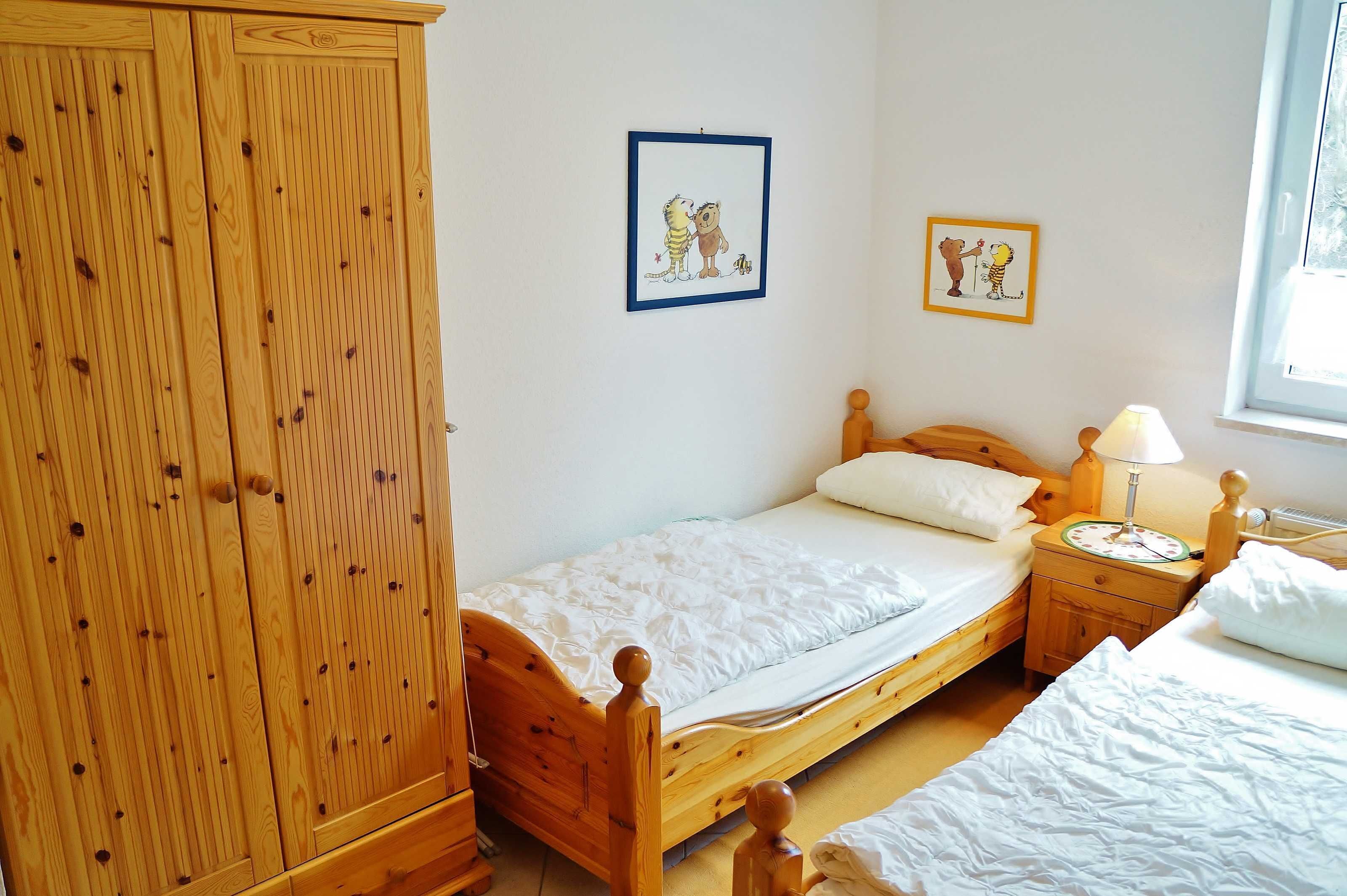 Un dormitorio con una cama de madera, una mesita de noche con una lámpara y dos cuadros en la pared.