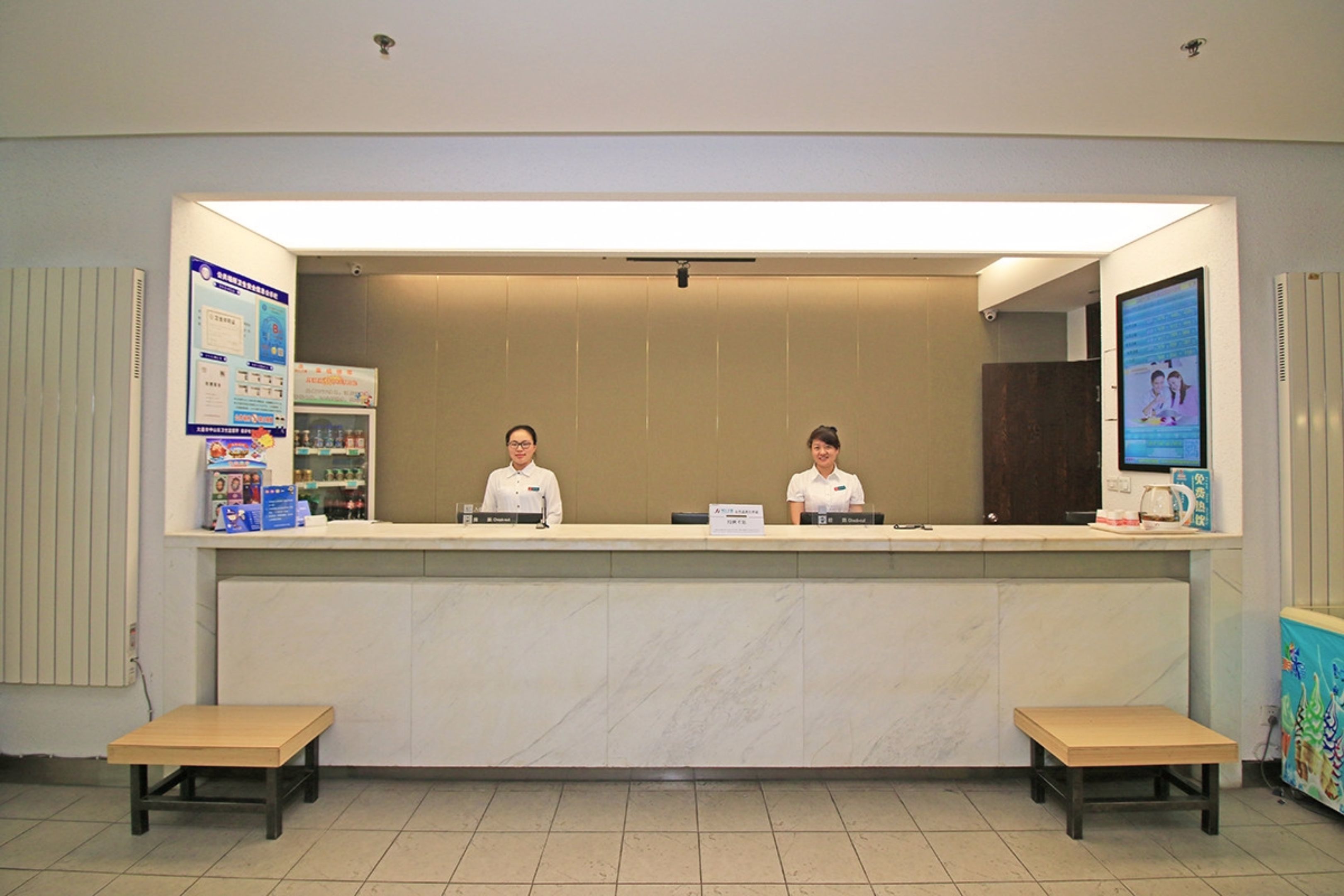 A reception desk with two staff members, a bulletin board, and a vending machine.