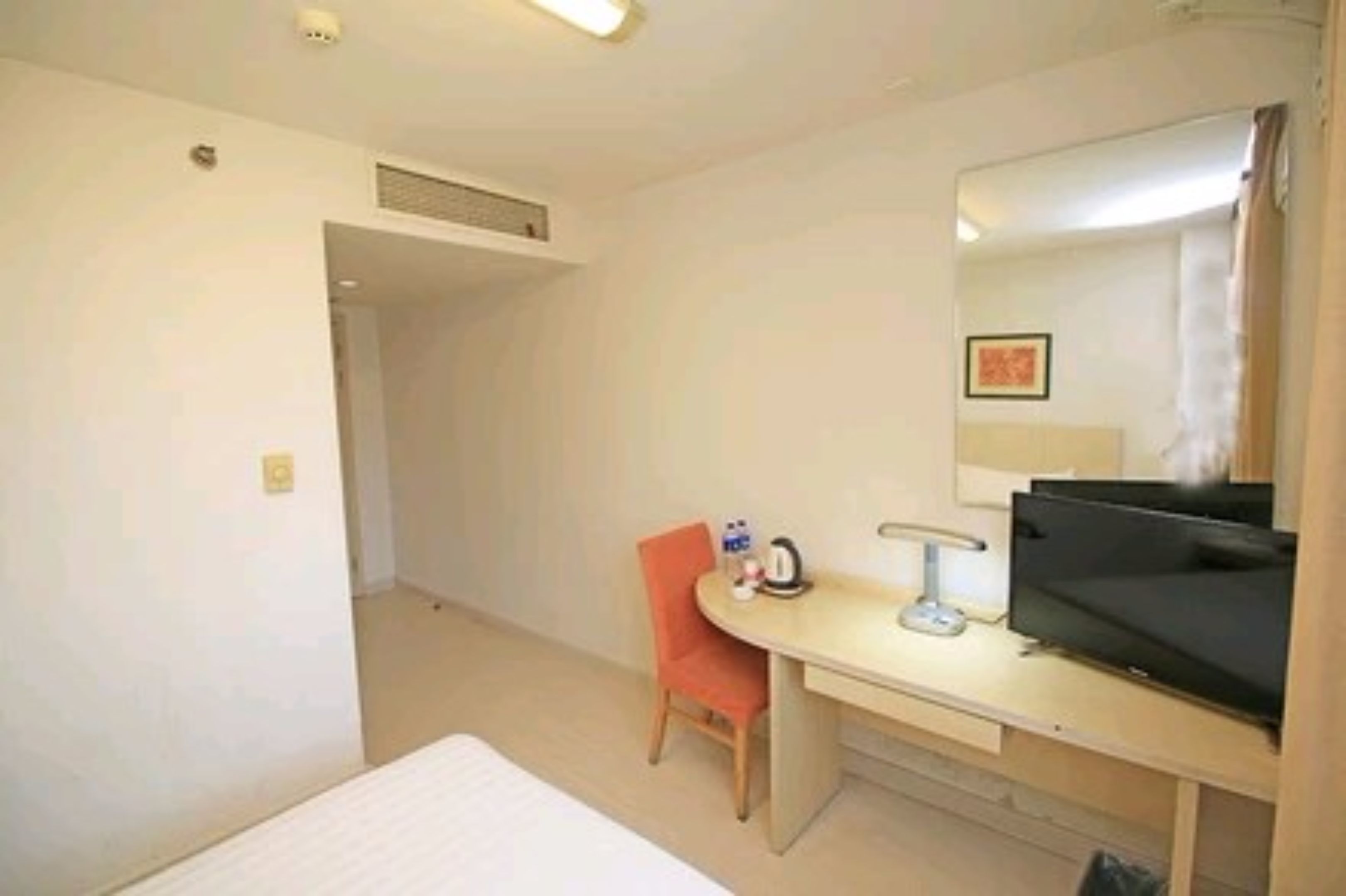 A hotel room with a bed, a desk with a chair, a television, and a mirror.