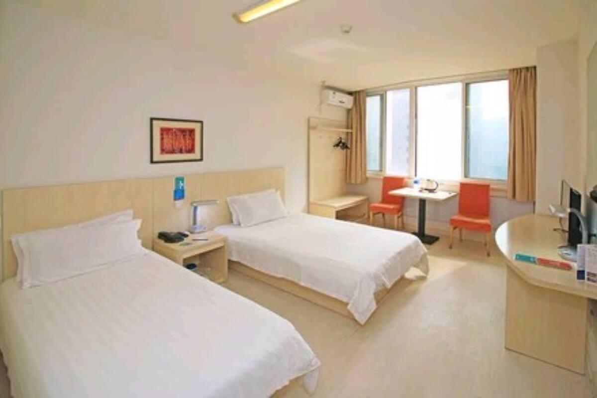 A hotel room with two beds, a desk, a chair, a TV, and a window with curtains.