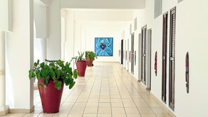A hotel corridor with potted plants, a large painting on the wall, and a tiled floor. - CityBlue Creekside Hotel & Suites, Mombasa (Mombasa)