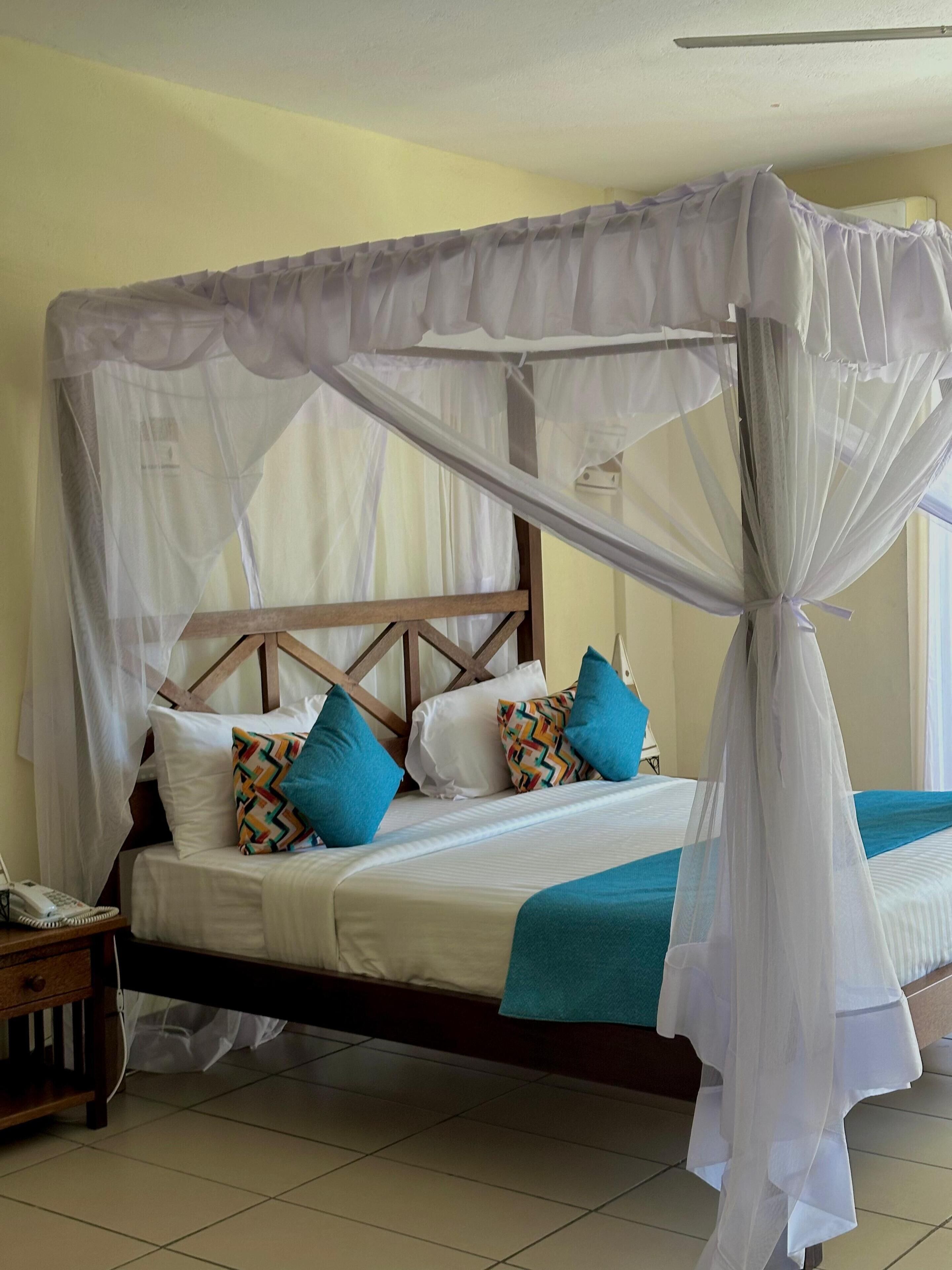 A bed with a canopy, pillows, a bedside table, and a telephone.
