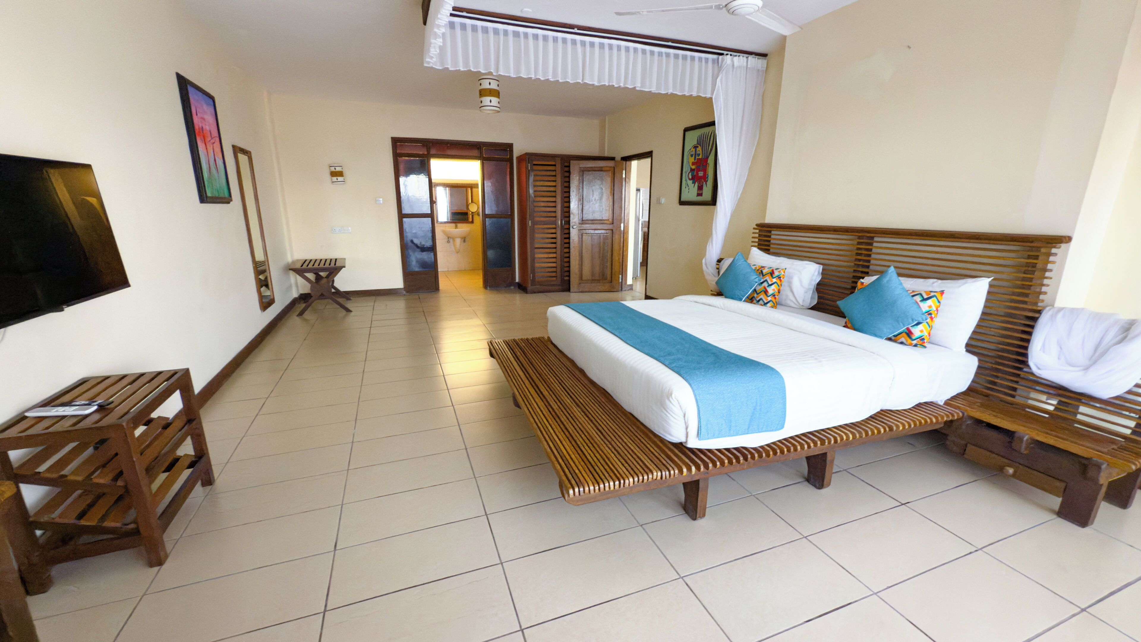 Habitación de hotel con cama, muebles de madera, televisor y baño visible a través de una puerta abierta.
