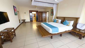 Habitación de hotel con cama, muebles de madera, televisor y baño visible a través de una puerta abierta.