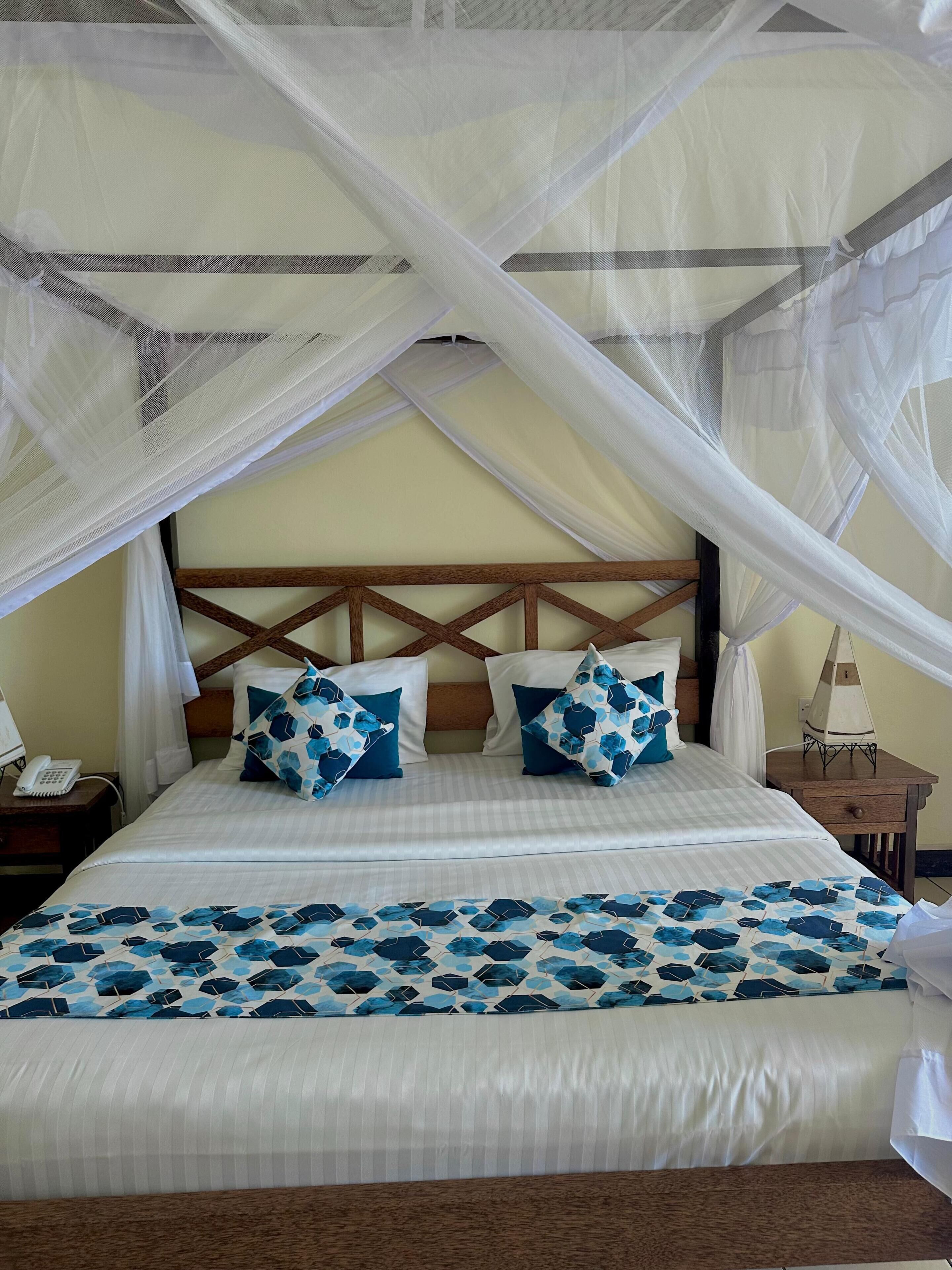 A bed with a canopy, pillows, a bedside table, and a wall-mounted phone.