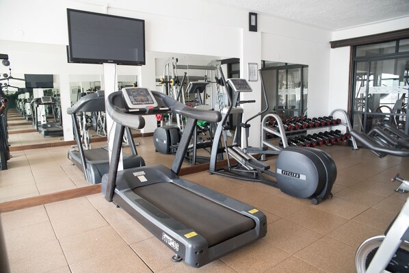 Une salle de sport équipée de tapis de course, de vélos elliptiques et d’haltères.