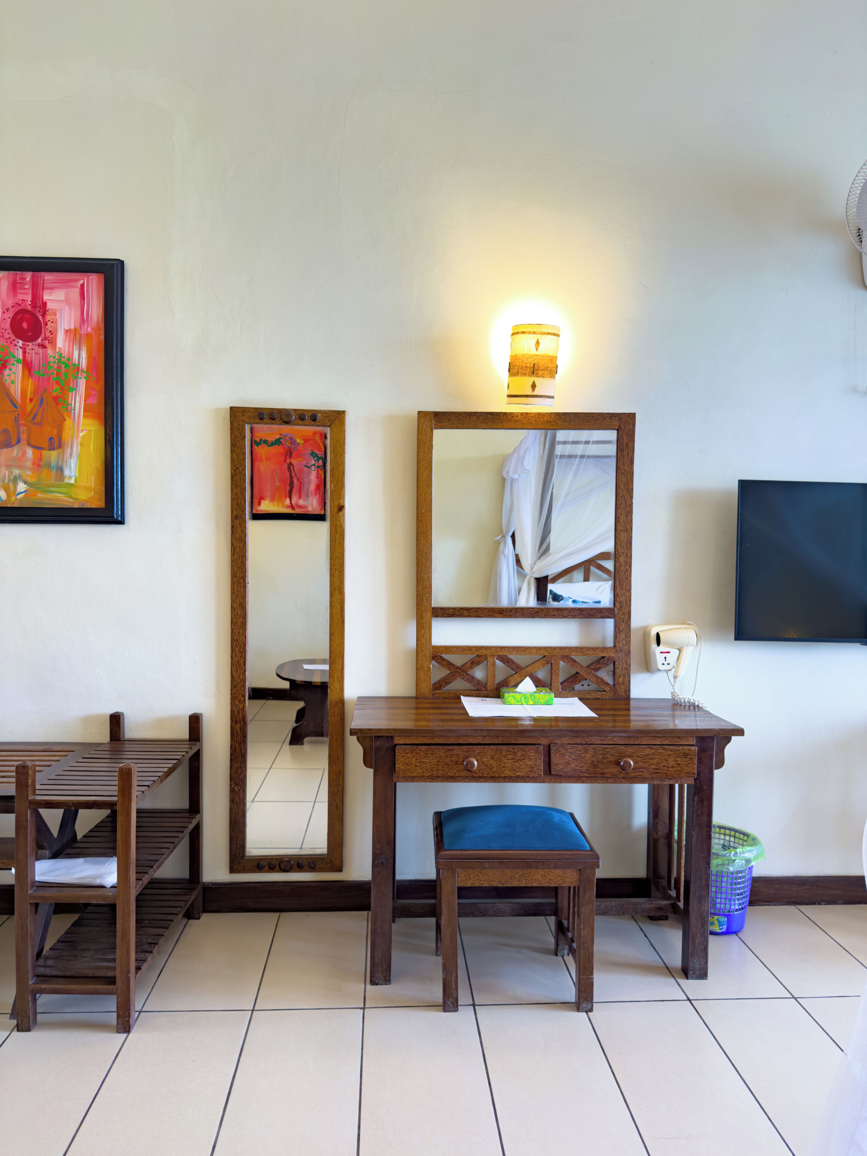 A room with a wooden desk, a chair, a mirror, and a television on the wall.