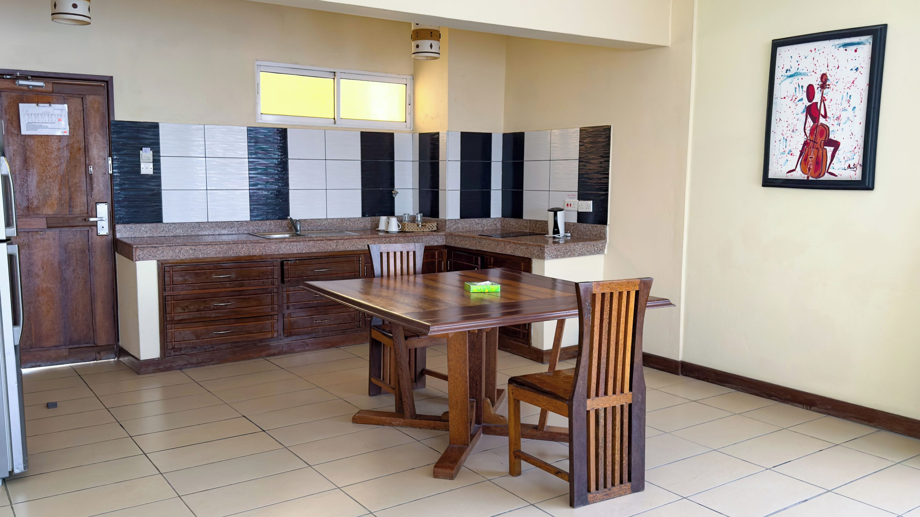 Een keuken met een houten tafel en stoelen, een raam en een schilderij aan de muur.