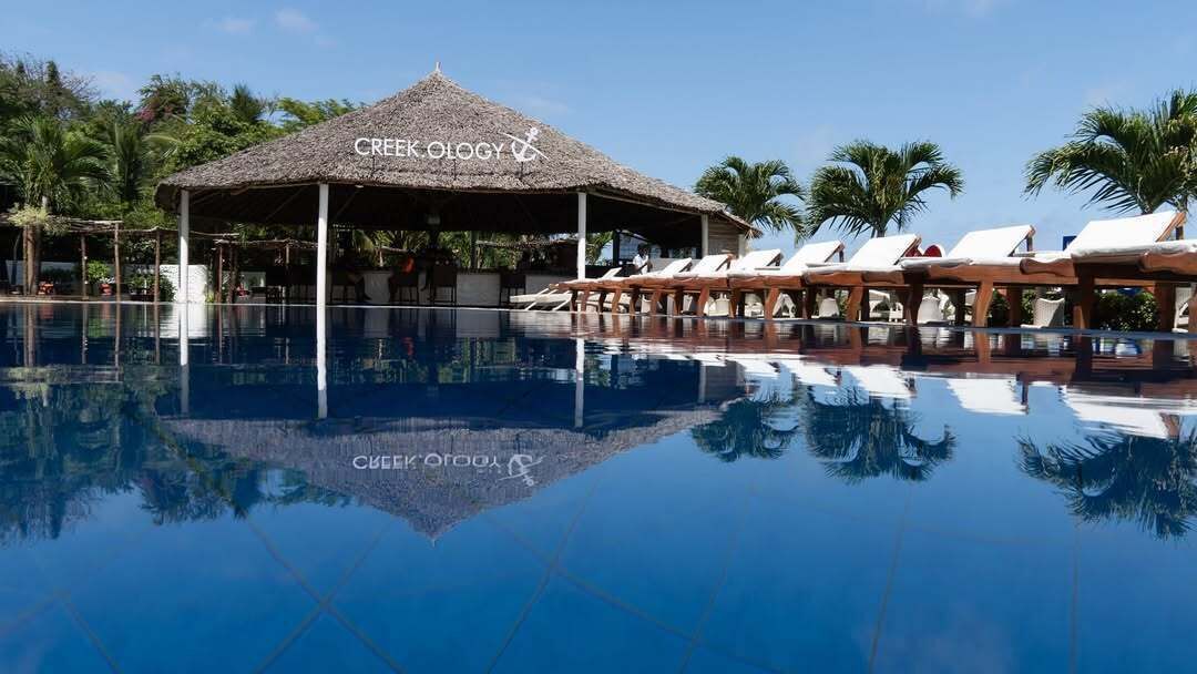 A pool area with lounge chairs and a thatched-roof structure labeled 'CREEK OLOGY'.