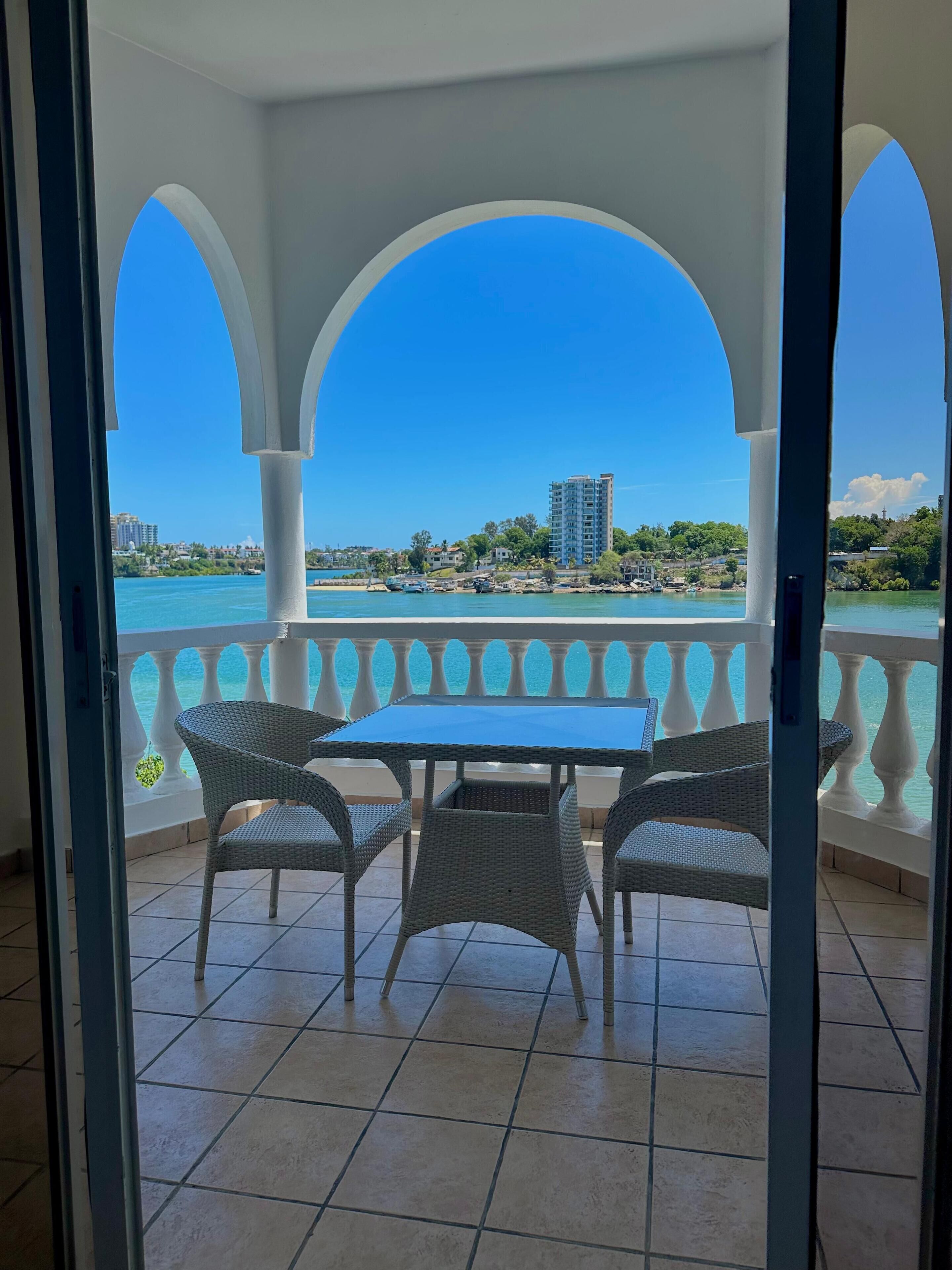 Varanda com vista para a água, uma mesa e cadeiras de vime.