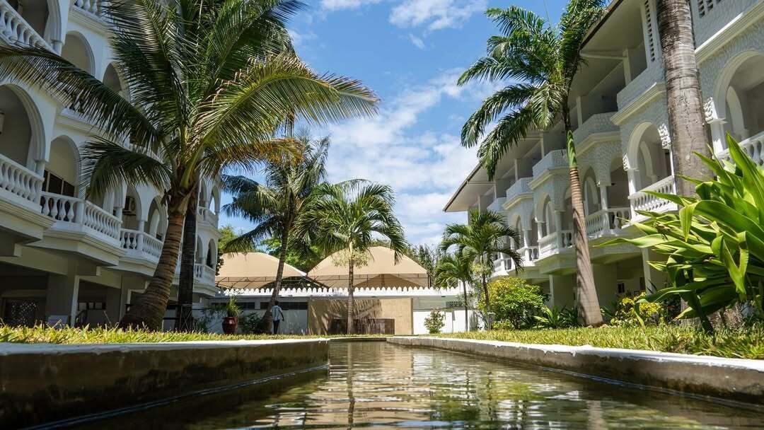 A hotel courtyard with a central water feature, palm trees, and multi-story buildings with balconies.