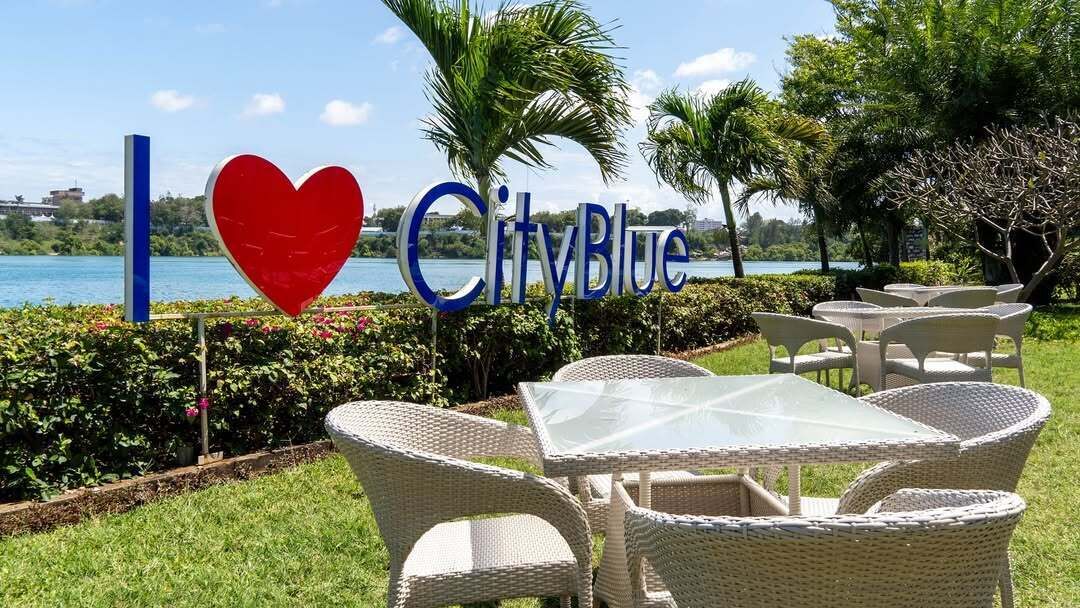 Ein Sitzbereich im Freien am Wasser mit Korbmöbeln und einem Schild mit der Aufschrift 'I love CityBlue'.