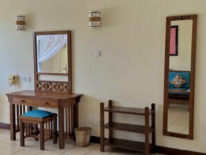A wooden desk with a chair, a mirror, and a shelf unit against a wall.