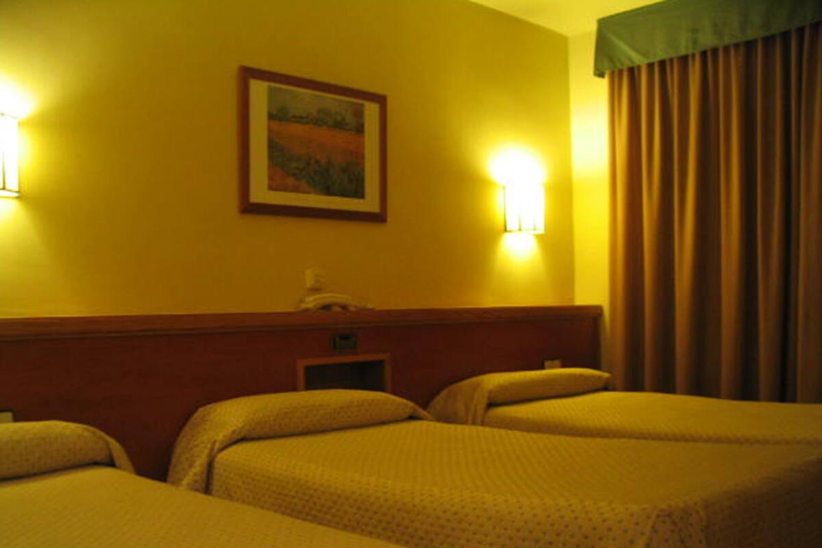 A hotel room with two beds, a painting on the wall, and a window with curtains.
