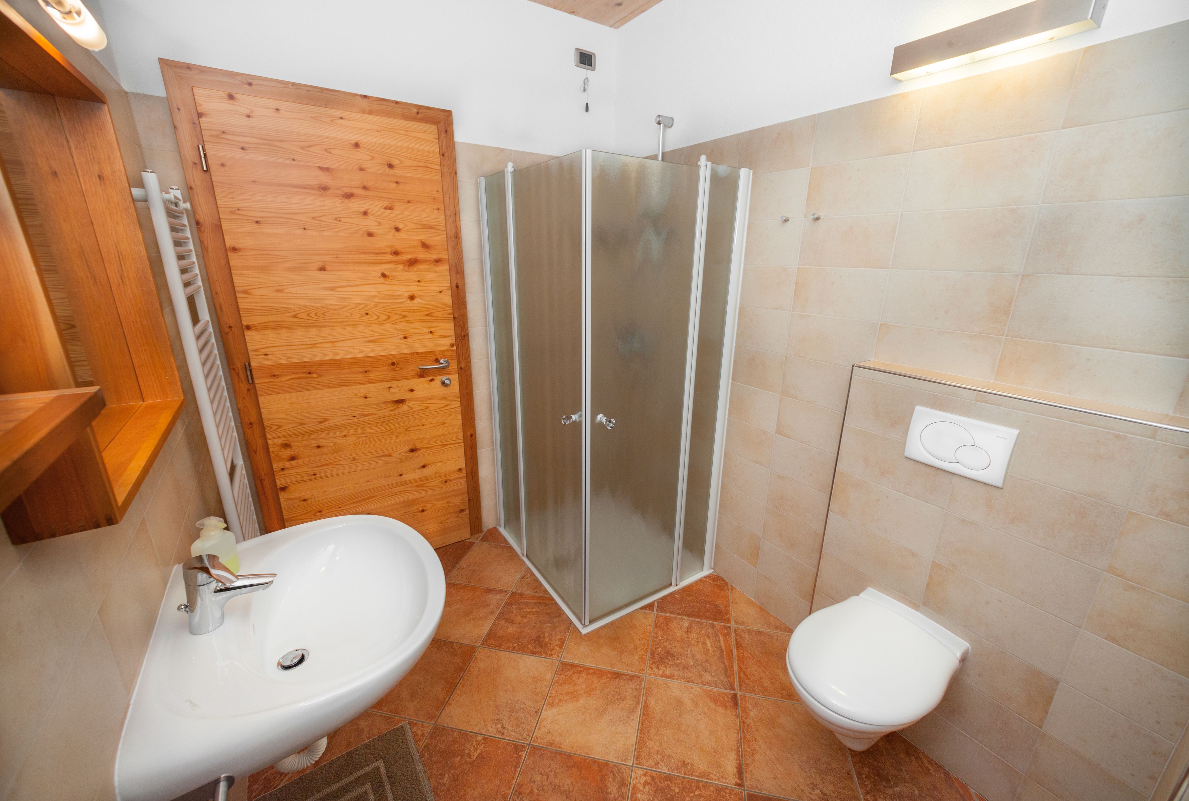 Un baño con puerta de madera, cabina de ducha con mampara de vidrio, lavabo e inodoro.