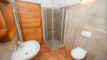 Un baño con puerta de madera, cabina de ducha con mampara de vidrio, lavabo e inodoro.