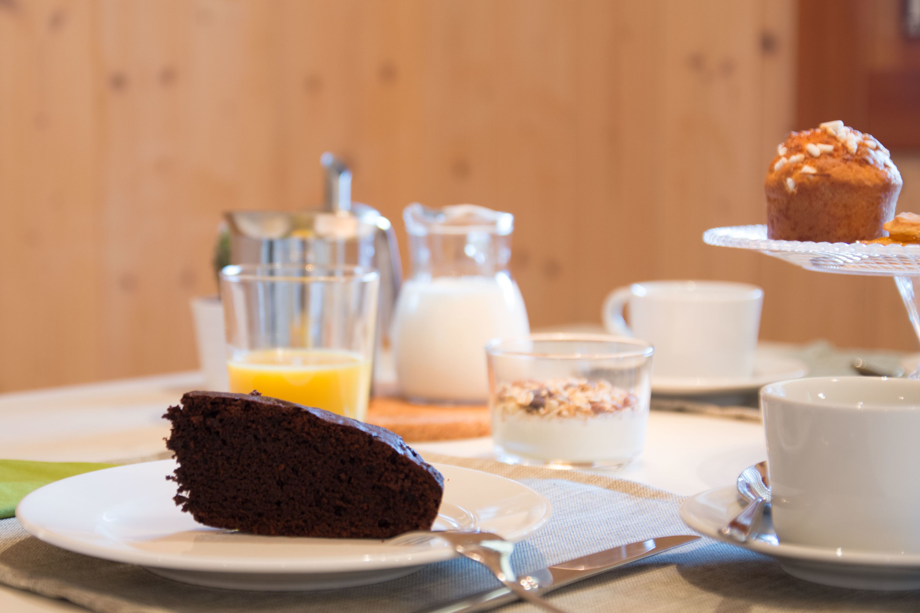 A breakfast setting with a slice of chocolate cake, a muffin, and a glass of orange juice on a table.