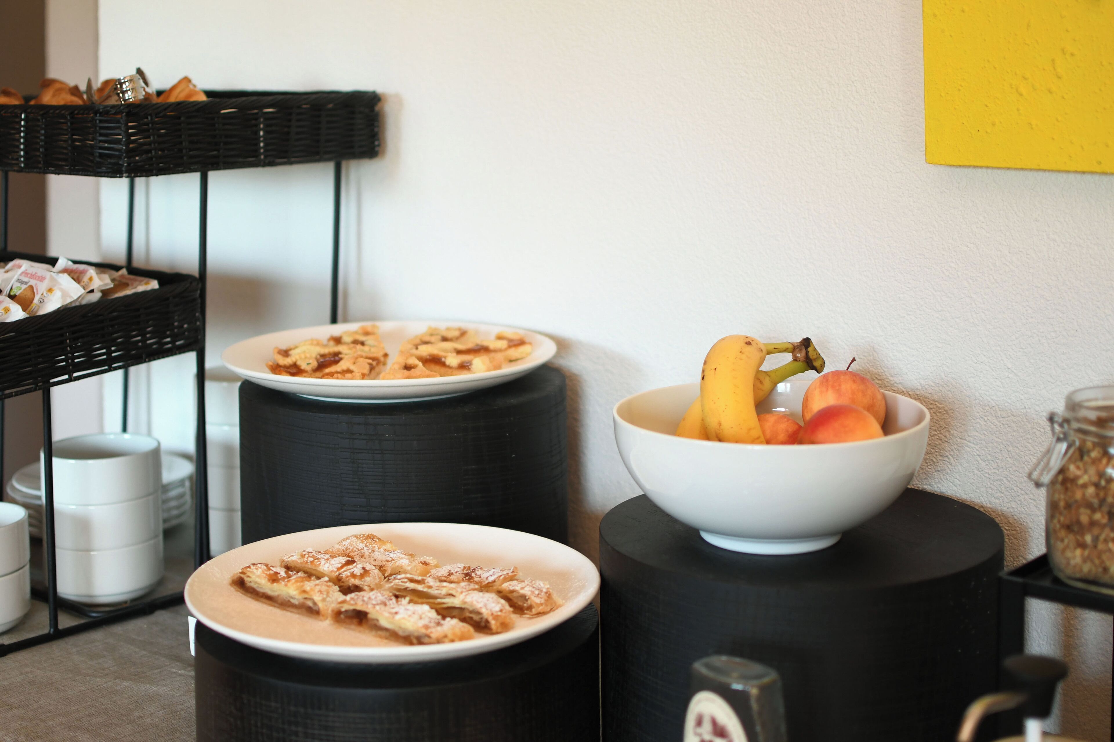 A breakfast setup with plates of pastries and a bowl of fruit on black stools.