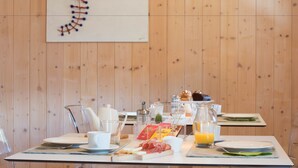 A breakfast table set with plates, glasses, and food items, with a wooden wall and a DNA helix artwork in the background. - Agritur Casteller (Trento)