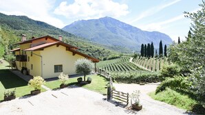 A yellow building with a red roof, surrounded by a well-maintained garden and a vineyard. - Agritur Casteller (Trento)