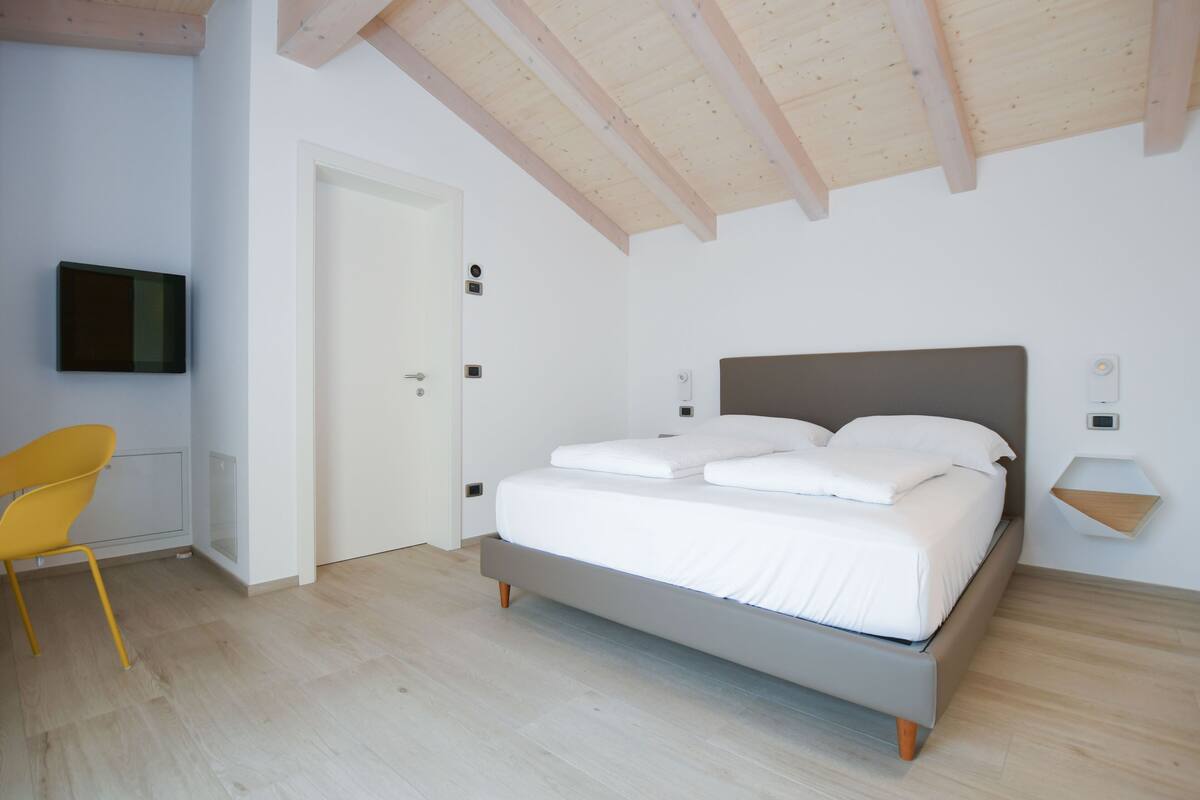 A bedroom with a bed, a chair, and a television mounted on the wall.