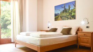 A bedroom with a wooden bed, white bedding, a nightstand, a wall-mounted light, and a window with curtains. - Agritur Casteller (Trento)