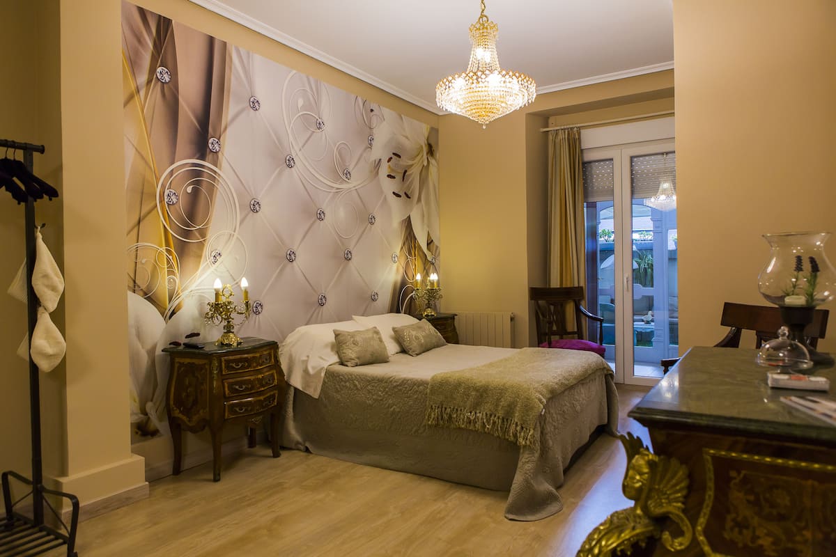 A bedroom with a large bed, a chandelier, a dresser, and a view of the outdoors through a glass door.