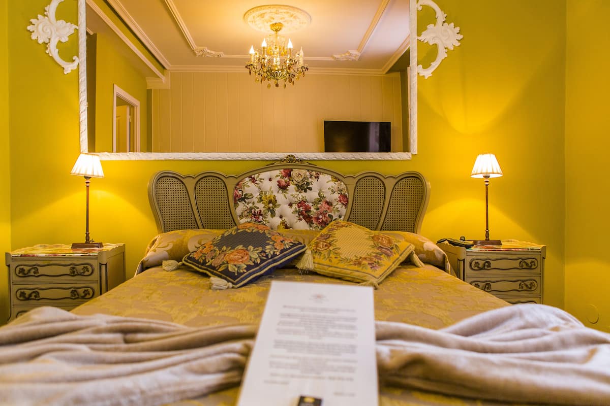 A neatly made bed with floral pillows, a mirror, and two bedside tables with lamps.