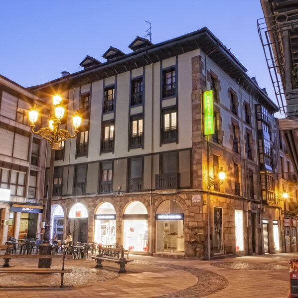 Un edificio histórico con varias tiendas, un patio central con bancos y un letrero iluminado y llamativo.
