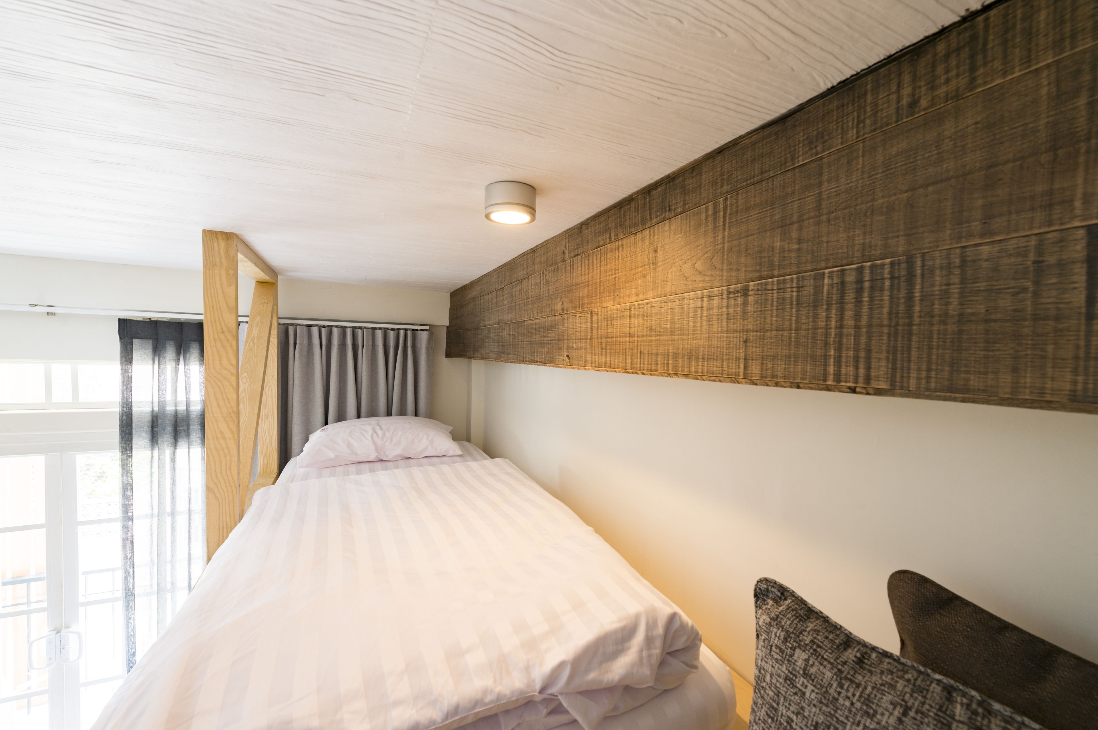 A bedroom with a bed, a wooden headboard, a window with curtains, and a ceiling light.