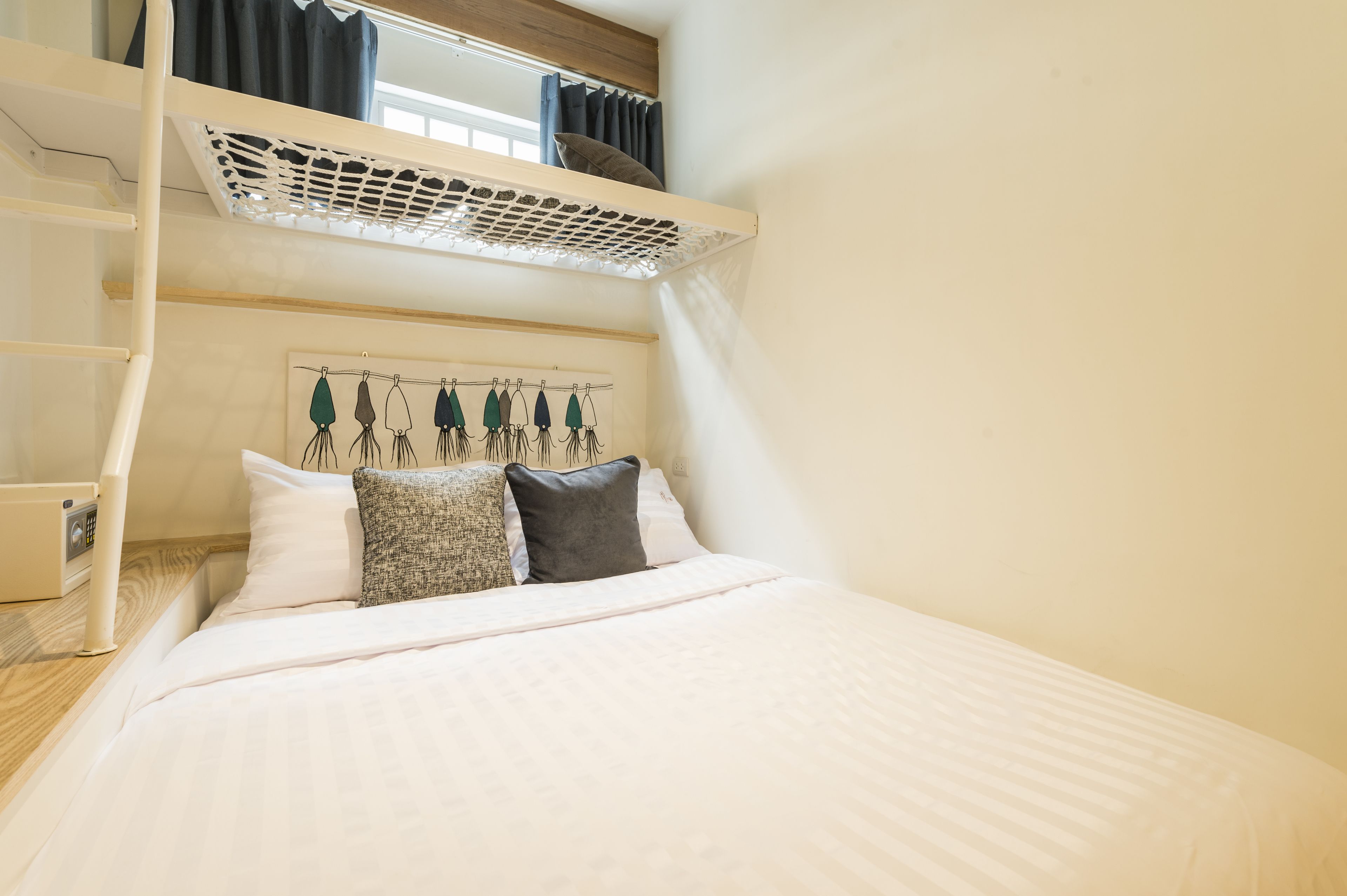 Una cama litera con dosel blanco, una mesita de noche y un tendedero de pared con toallas.