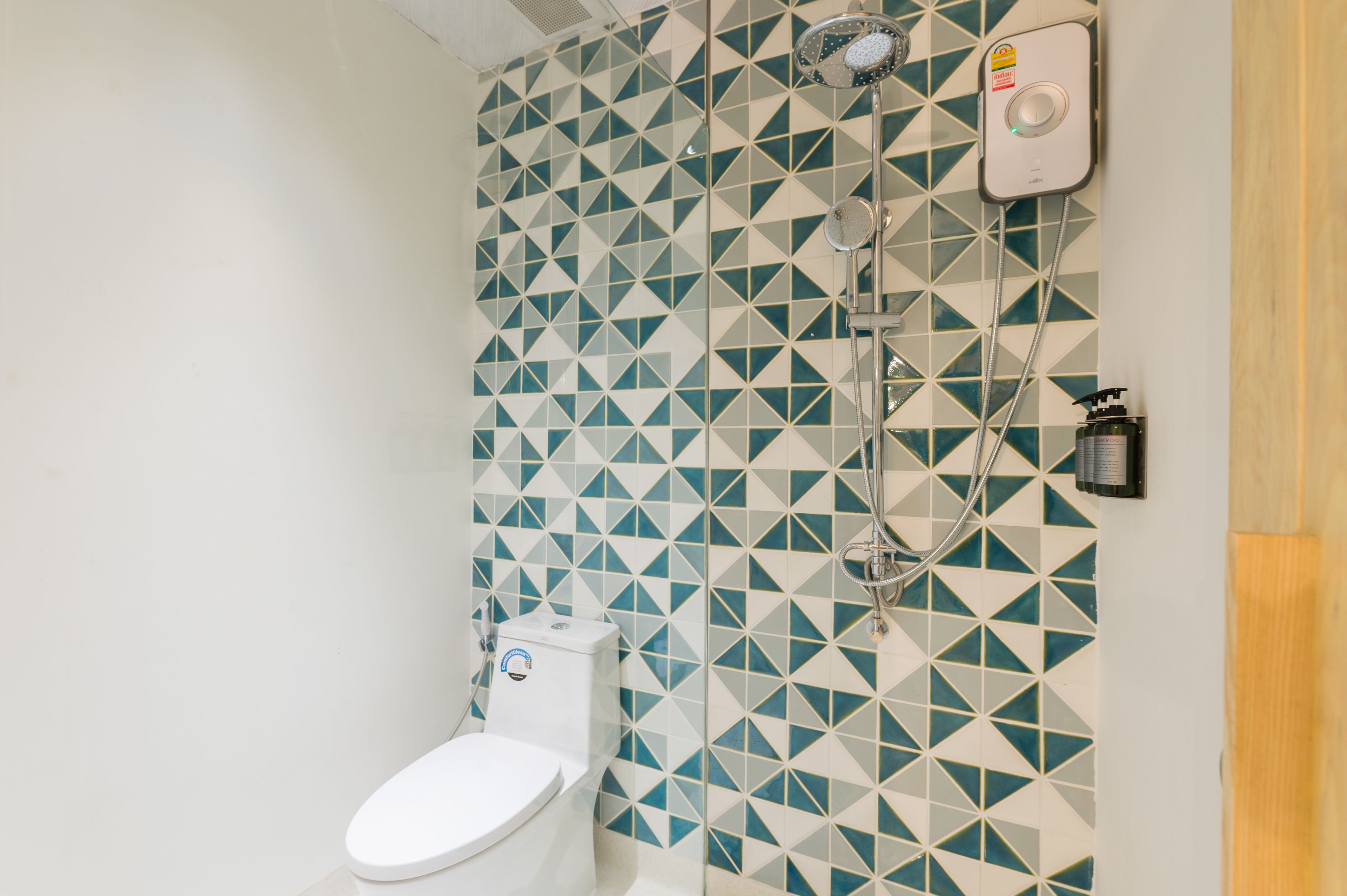 A bathroom with a white toilet, a shower with a handheld showerhead, and a wall-mounted control panel.