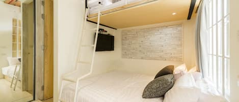 A bunk bed with a ladder, a white bedspread, and pillows. There is a window with curtains and a wall with a patterned design.