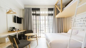 Quarto de hotel com uma cama de solteiro, uma mesa com cadeira, uma mesinha e uma televisão fixada na parede.