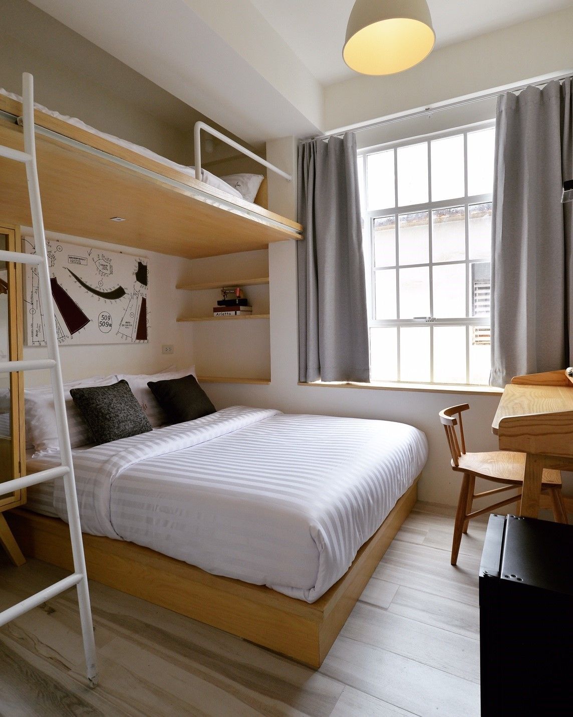A bunk bed room with a desk, a ladder, and a window with curtains.