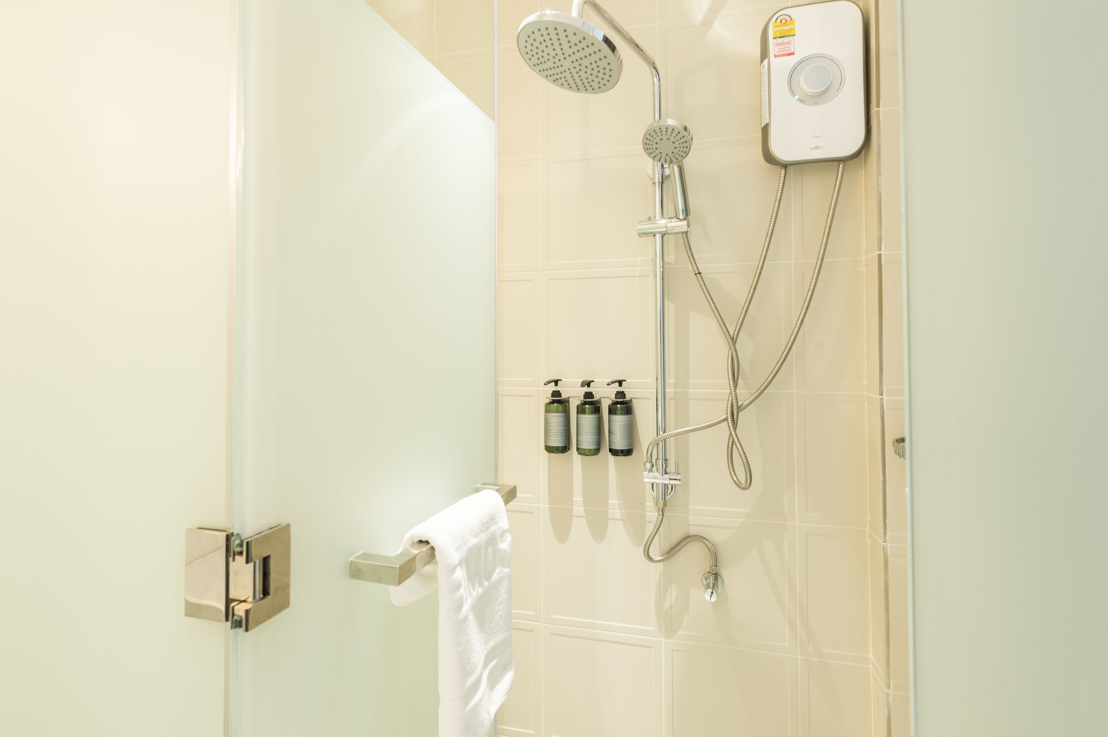 A modern bathroom with a glass shower enclosure, a handheld showerhead, a wall-mounted control panel, and three bottles of toiletries.