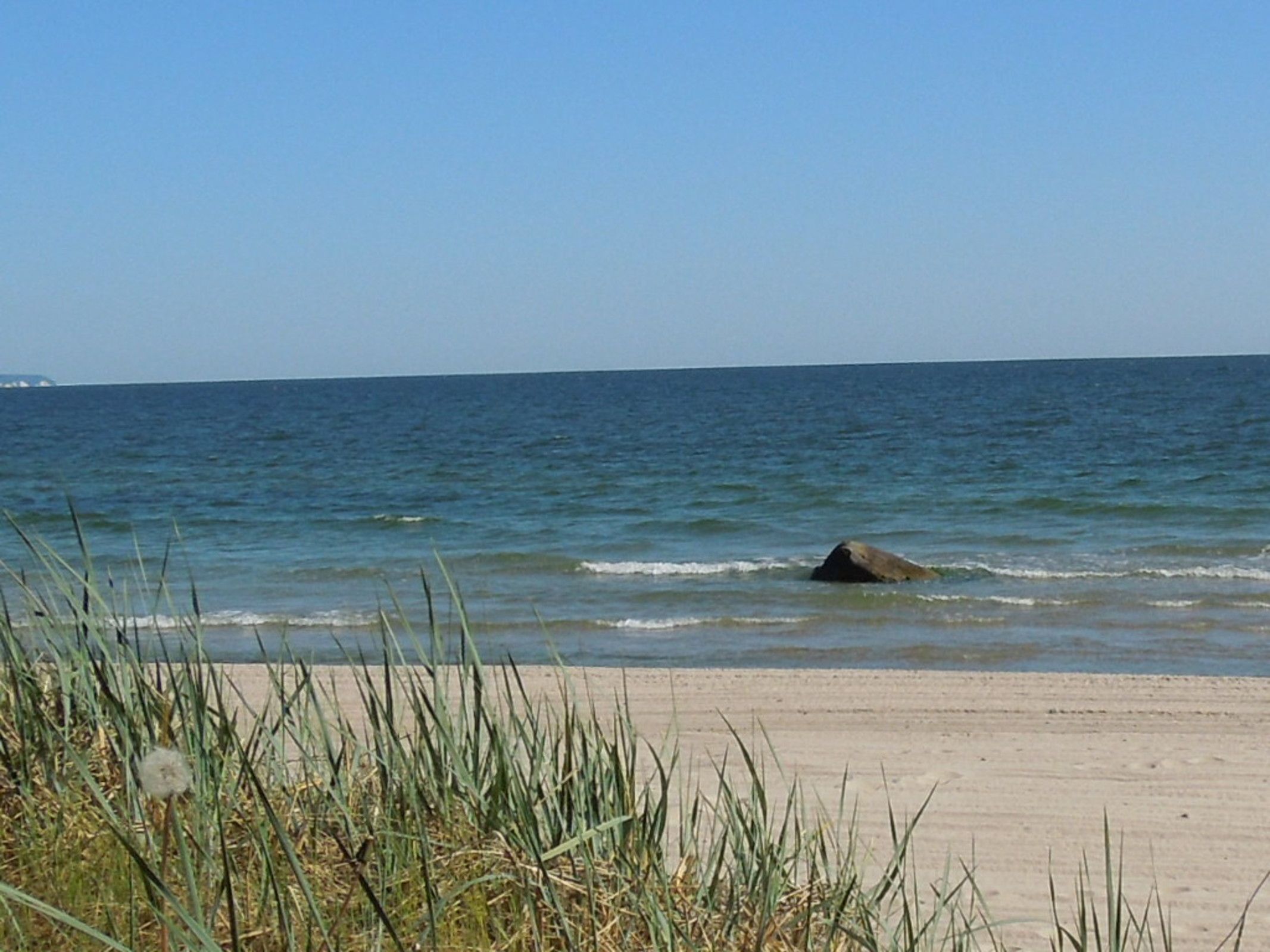 Ein Strand mit klarem Himmel, ruhigem Wasser und sandigem Ufer.