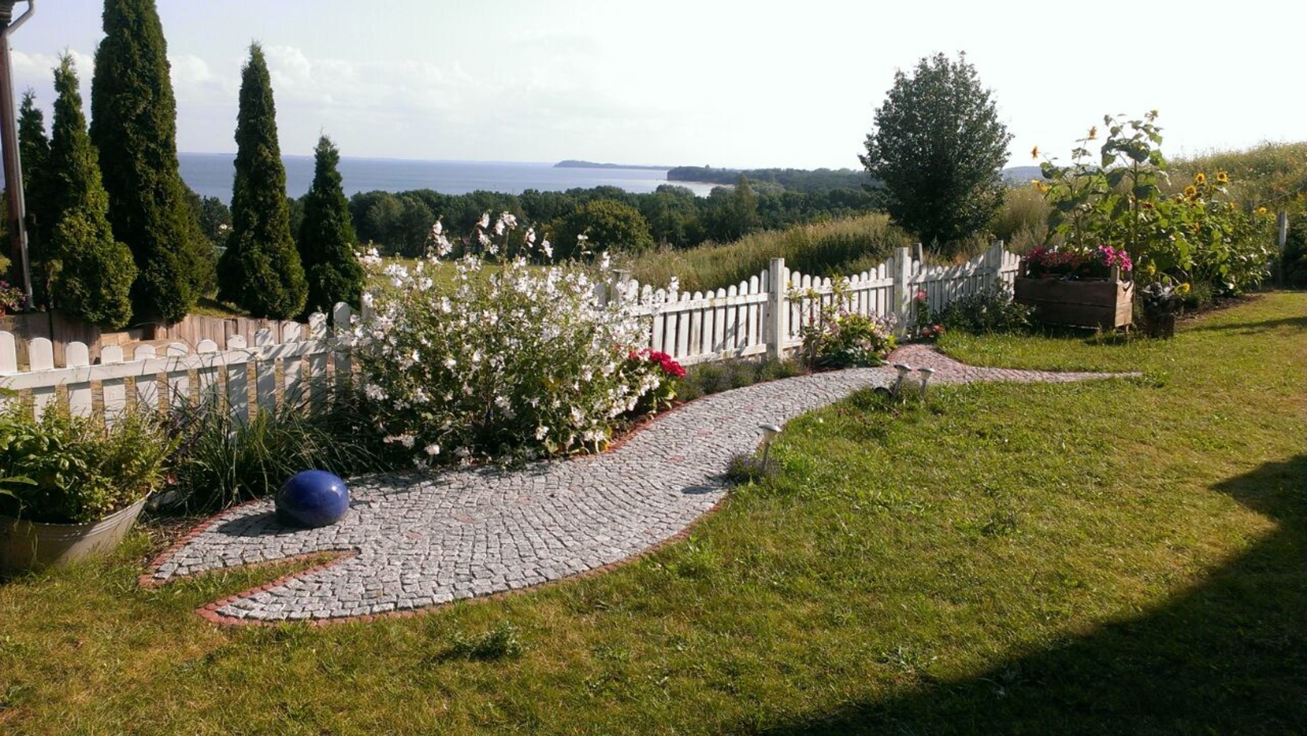 Ein Garten mit einem Kopfsteinpflasterweg, einem weißen Ziergartenzaun und verschiedenen Pflanzen.