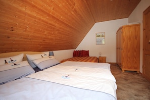 A bedroom with a sloped ceiling, two beds with matching bedding, a wooden wardrobe, and a small bedside table with a lamp.