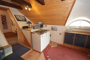 A compact kitchen with a microwave, toaster, and small refrigerator. There is a wooden staircase leading to another room, and a window with a view of the outside.