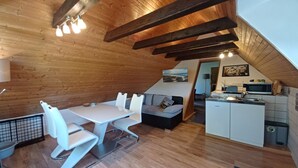 A cozy attic-style room with a dining table, chairs, a sofa, and a kitchenette.